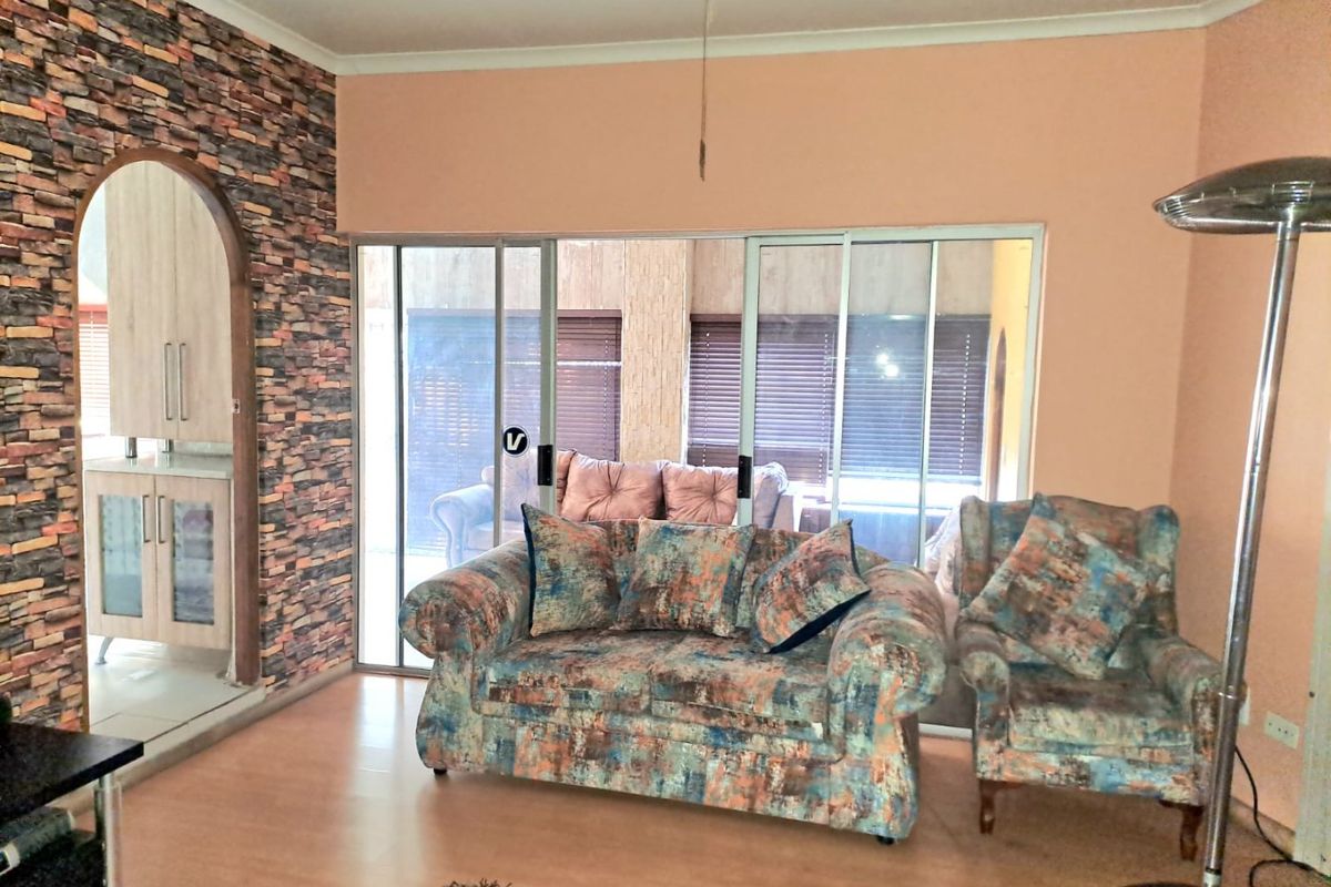 A living room featuring a stone-effect feature wall, arched doorway leading to the kitchen, and large sliding glass doors providing access to the patio.