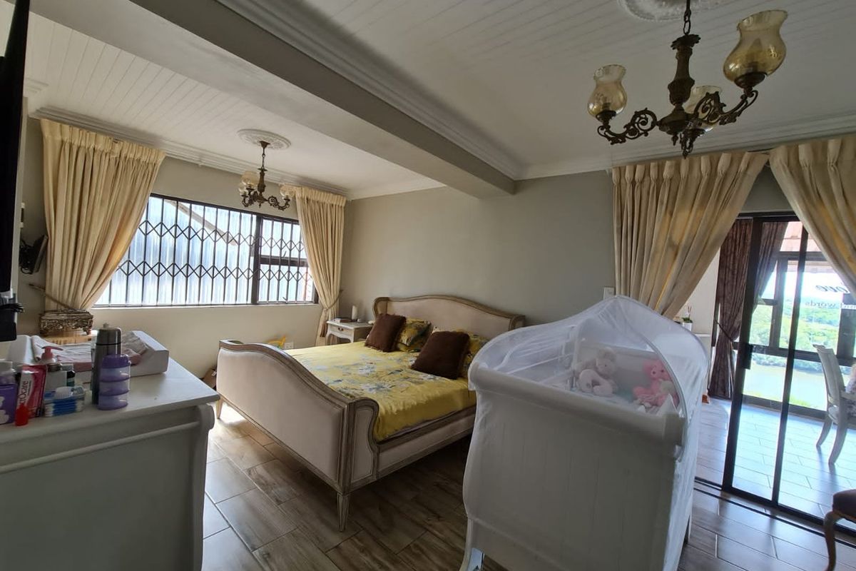 Spacious bedroom featuring wood-look tile flooring, decorative ceiling cornices, dual chandeliers, and direct access to an outdoor patio area.