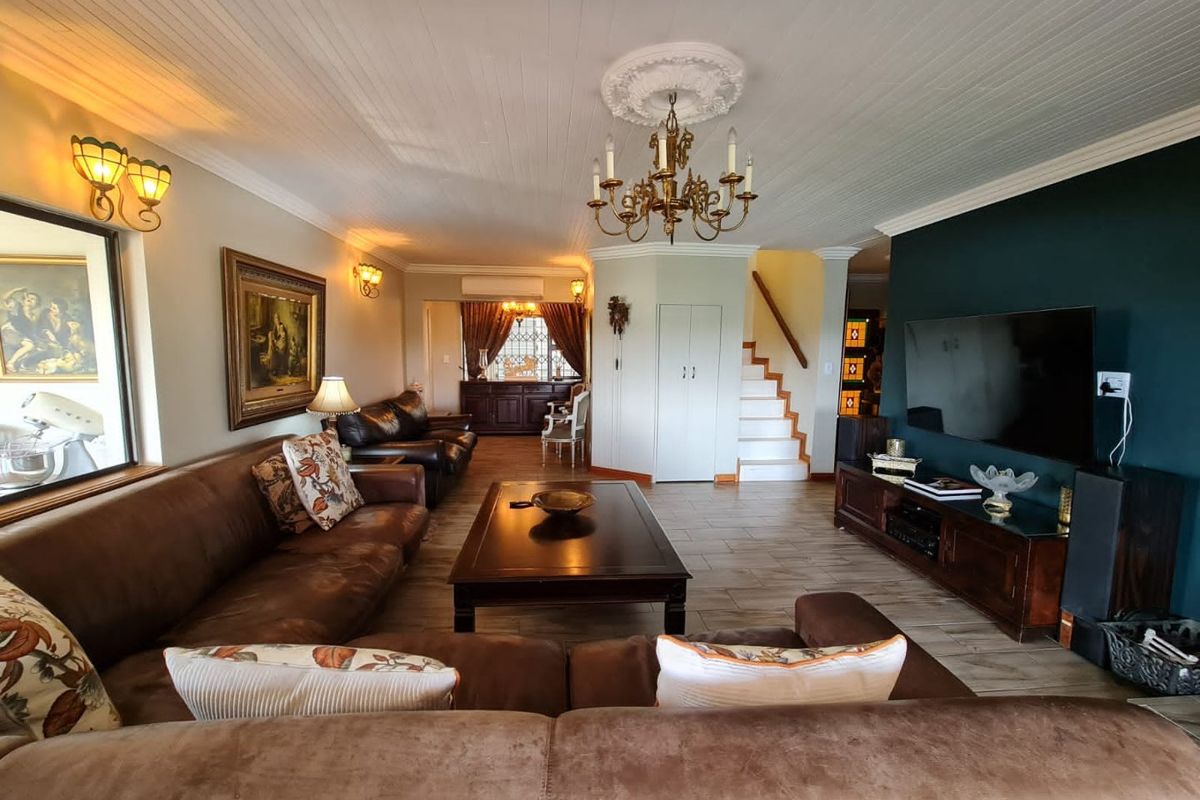 Spacious living room featuring a classic chandelier, decorative ceiling rose, tiled flooring, and a feature wall with built-in television mounting.