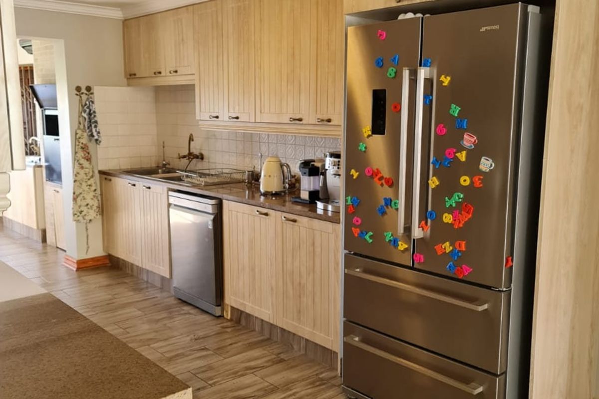 A functional kitchen featuring light wood-grain cabinetry, stone-look countertops, tiled flooring, and a built-in refrigerator housing.