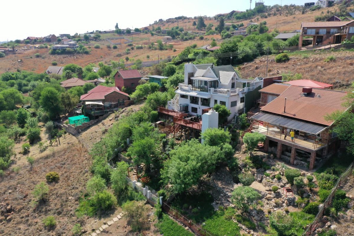 Aerial view of a multi-level residential property featuring tiered wooden decking, a prominent chimney, and landscaped garden areas set within a hilly landscape.