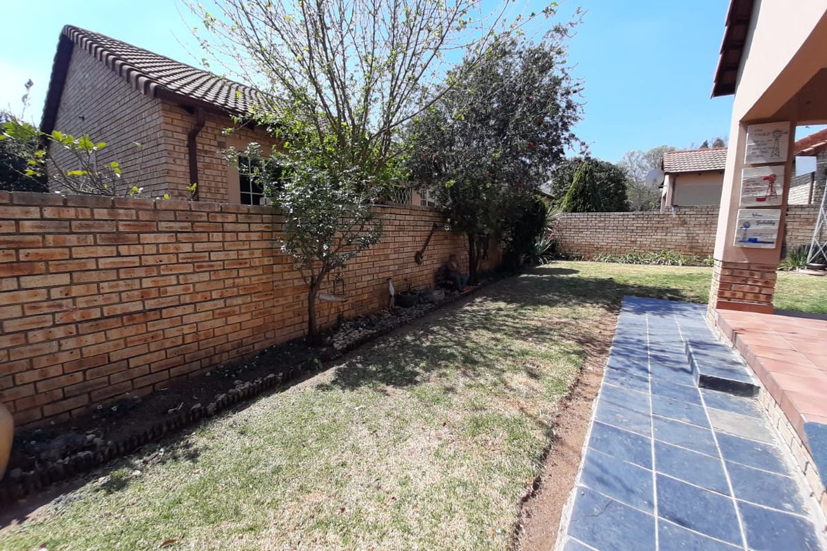 A private rear garden featuring a tiled patio area, brick boundary walls, and established trees, offering a quiet outdoor space for the townhouse.