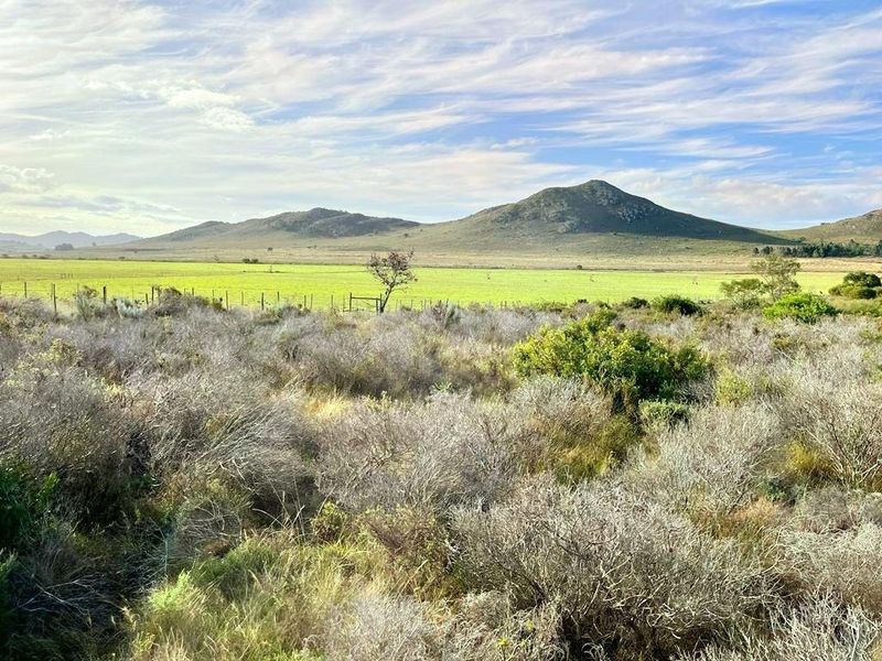 A scenic view of open vacant land featuring natural vegetation, wire fencing, and distant mountain ranges under a clear sky.