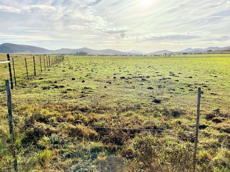 Expansive view of open residential land featuring wire fencing and distant mountain ranges under a bright sky.