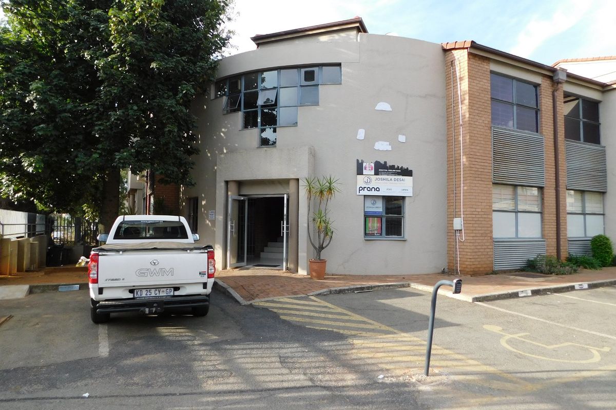 Front exterior view of a commercial office building featuring a paved parking area, brick and plastered facade, and main entrance access.