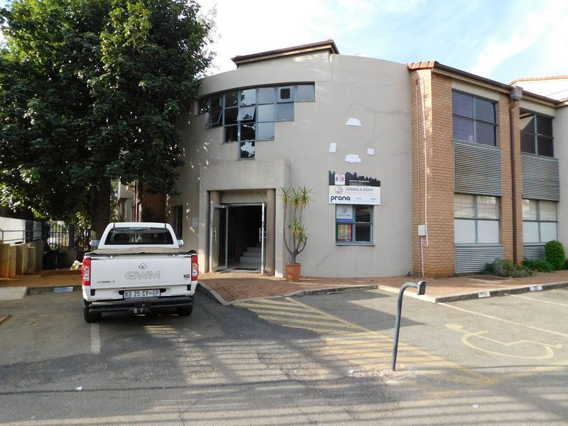 Front exterior view of a commercial office building featuring a paved parking area, brick and plastered facade, and main entrance access.