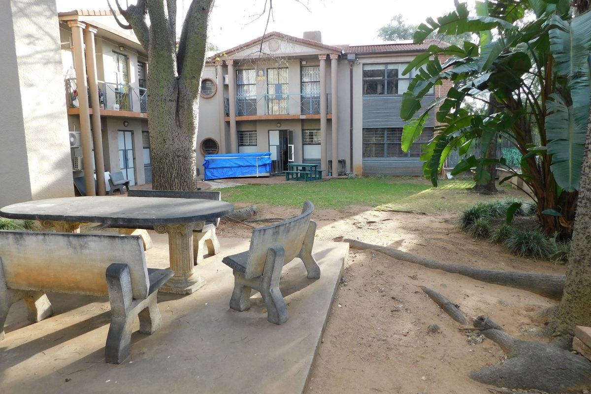 Rear exterior view of the office building featuring a concrete patio area, landscaped garden space, and multi-level balconies with security features.