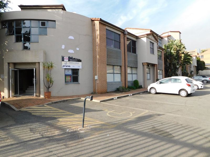 Front exterior view of a commercial office building featuring brick and plaster finishes, paved parking area, and designated disabled parking bays.