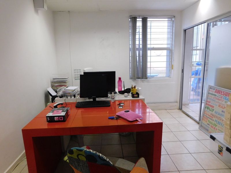 A functional office space featuring tiled flooring, a window with security bars, and a sliding glass door providing access to an outdoor area.