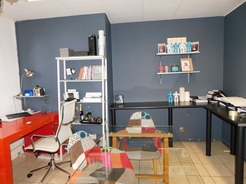 A functional office space featuring tiled flooring, a suspended ceiling, and built-in wall shelving, providing a practical work environment.