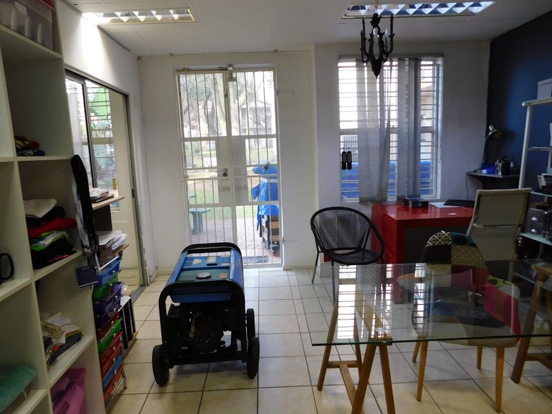 A functional office space featuring tiled flooring, recessed ceiling lights, and secure access points with security gates and window bars.