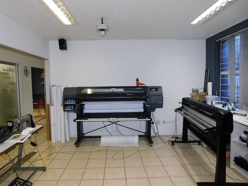 A functional office or production space featuring tiled flooring, fluorescent lighting, and security bars on the window.