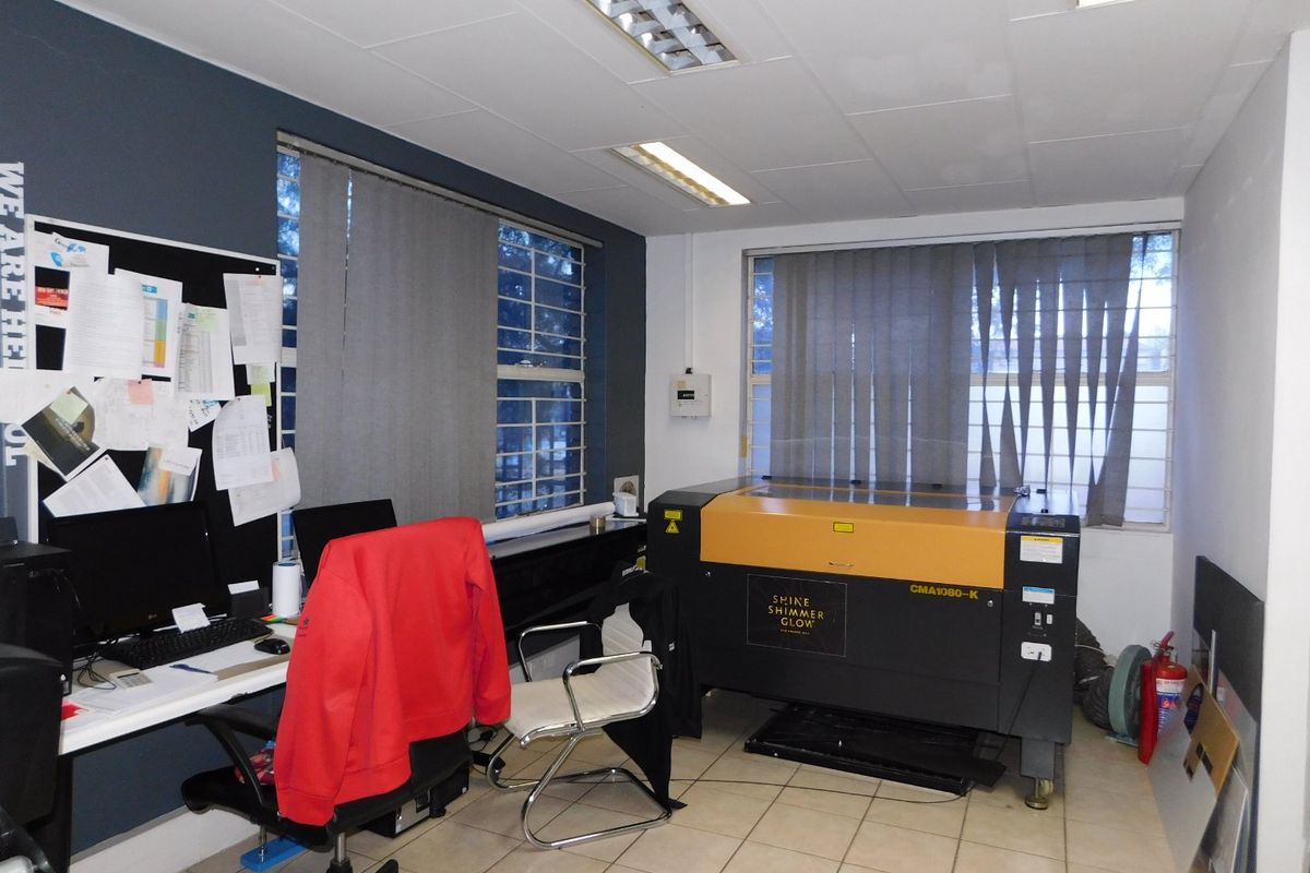 A functional office space featuring tiled flooring, vertical blinds, and security bars on the windows, suitable for professional use.
