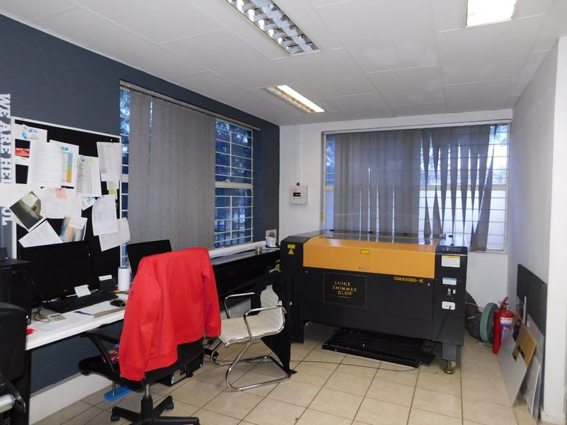 A functional office space featuring tiled flooring, vertical blinds, and security bars on the windows, suitable for professional use.
