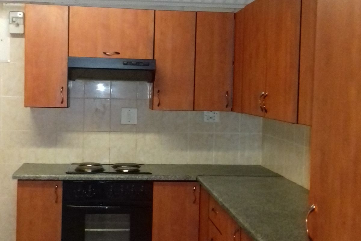 A functional kitchen featuring wood-finish cabinetry, tiled flooring, and built-in oven and hob appliances.