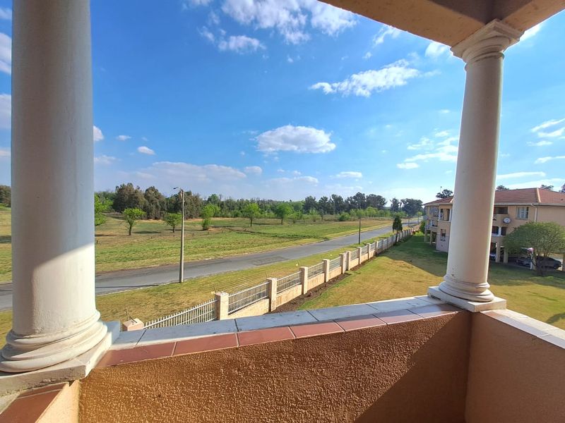 A covered balcony featuring decorative columns and tiled flooring, offering an elevated view of the surrounding landscape and neighborhood.