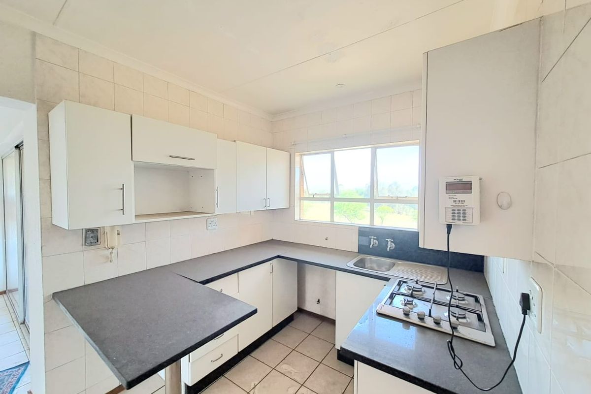 A functional kitchen featuring white built-in cabinetry, dark laminate countertops, a gas hob, and tiled finishes, offering a clean space ready for updates.