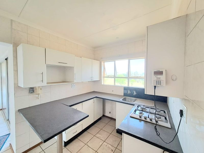 A functional kitchen featuring white built-in cabinetry, dark laminate countertops, a gas hob, and tiled finishes, offering a clean space ready for updates.