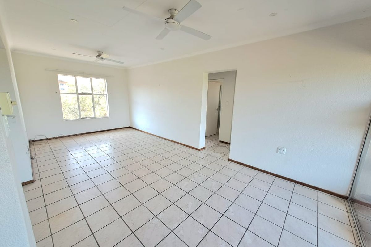 A spacious, empty living area featuring neutral tiled flooring, dual ceiling fans, and large windows providing natural light.