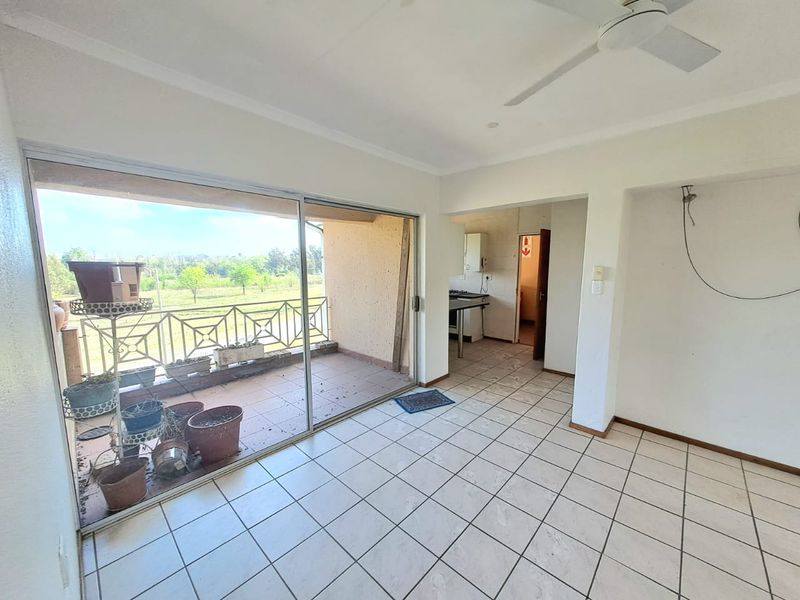 Open-plan living area featuring tiled floors, a ceiling fan, and large sliding doors leading to a balcony with scenic views.