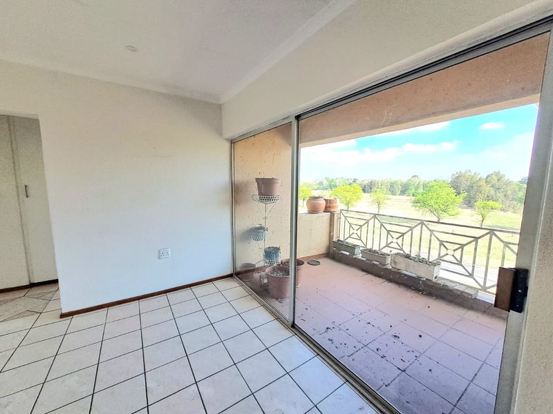 An empty balcony area featuring tiled flooring, a sliding glass door, and a metal balustrade with views of the surrounding landscape.