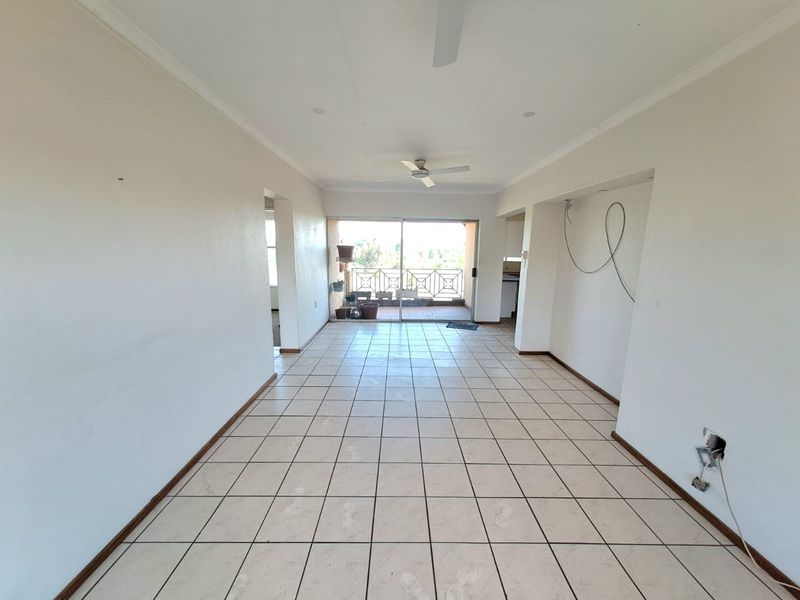 An empty open-plan living area featuring tiled floors, a ceiling fan, and direct access to a balcony through sliding glass doors.