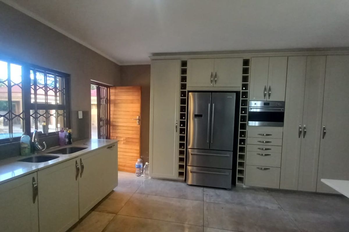 A well-appointed kitchen featuring extensive built-in cabinetry, integrated appliances, a double sink, and large format floor tiles with direct access to the exterior.