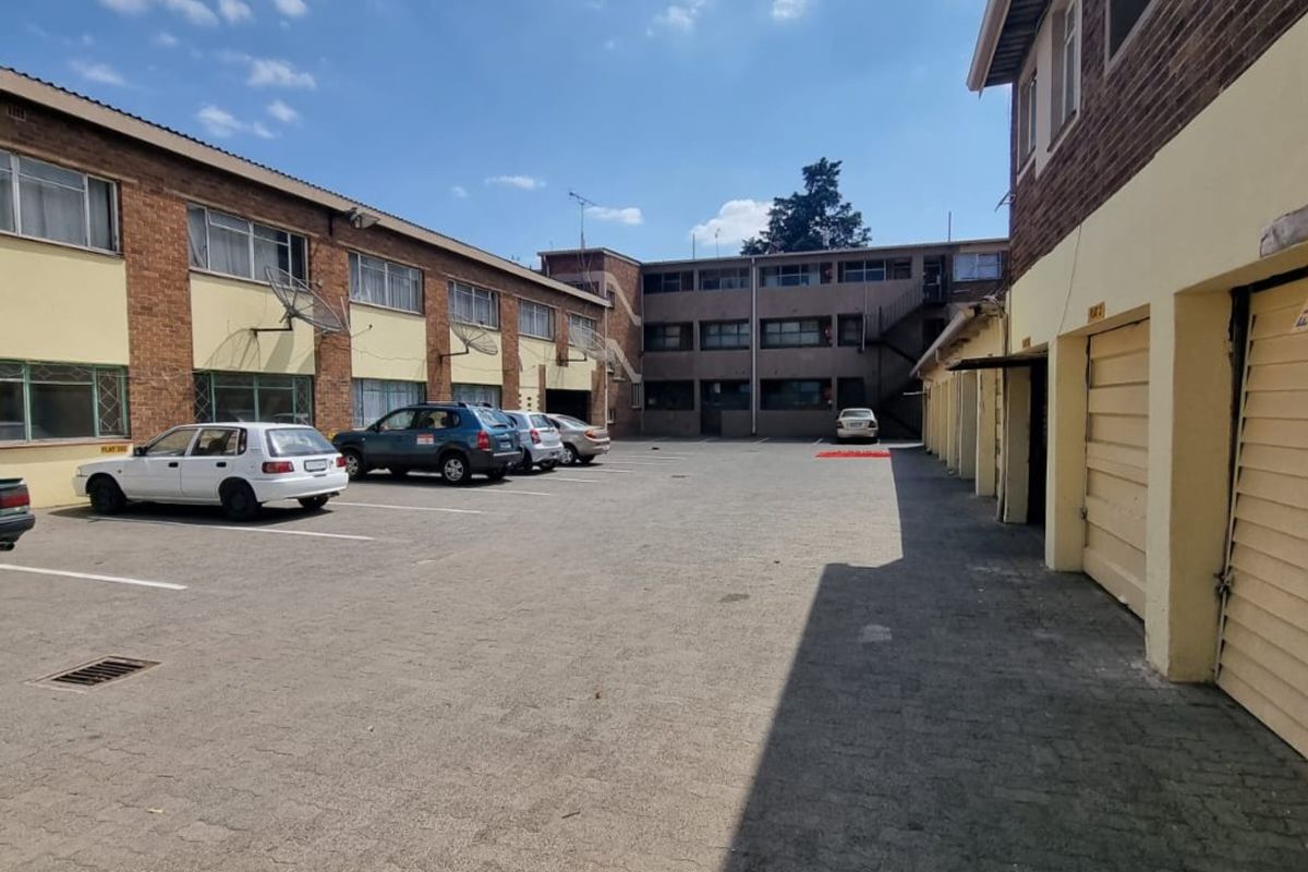 Exterior view of the apartment complex courtyard featuring paved parking area, multiple garage units, and brick facade building structure.