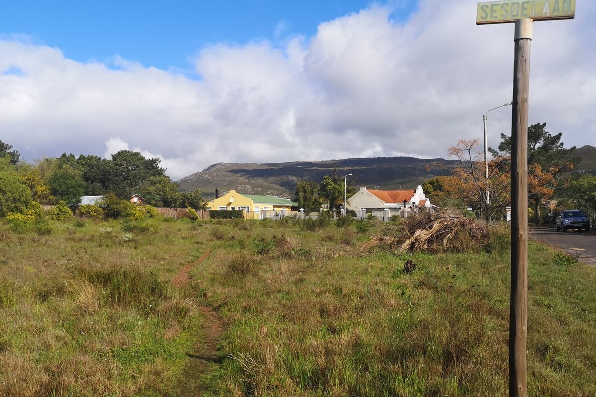 A view of a vacant residential plot featuring natural vegetation, with surrounding neighborhood houses and mountain views in the background.