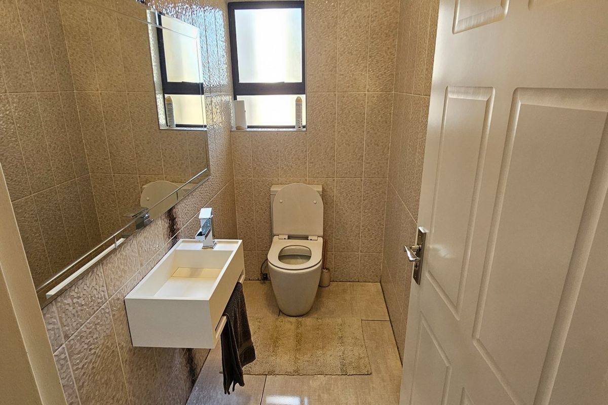 A compact guest bathroom featuring floor-to-ceiling wall tiles, a wall-mounted vanity basin, and a modern toilet.
