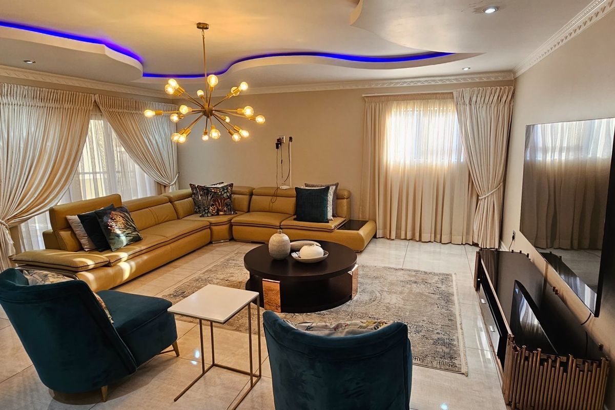 Spacious living room featuring a modern recessed ceiling with integrated LED lighting, tiled flooring, and large windows with floor-to-ceiling curtains.
