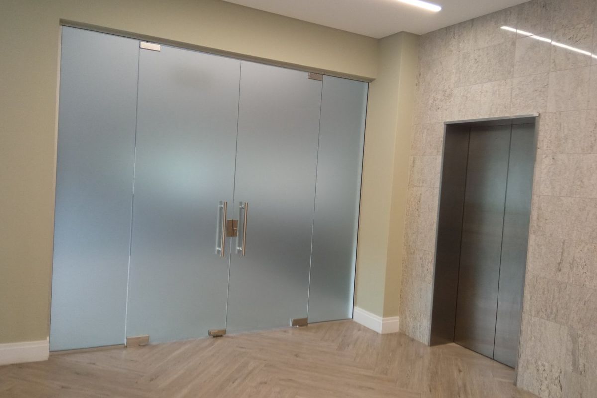 Modern office lobby area featuring frosted glass double doors, a stainless steel elevator, and elegant herringbone flooring with stone tile accents.