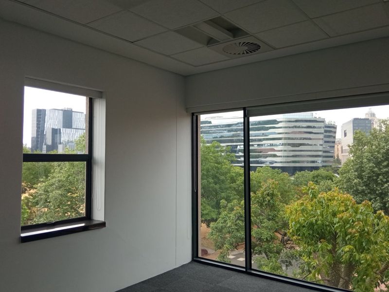 A bright, empty office space featuring a suspended ceiling, recessed air conditioning, and large windows offering an urban view.