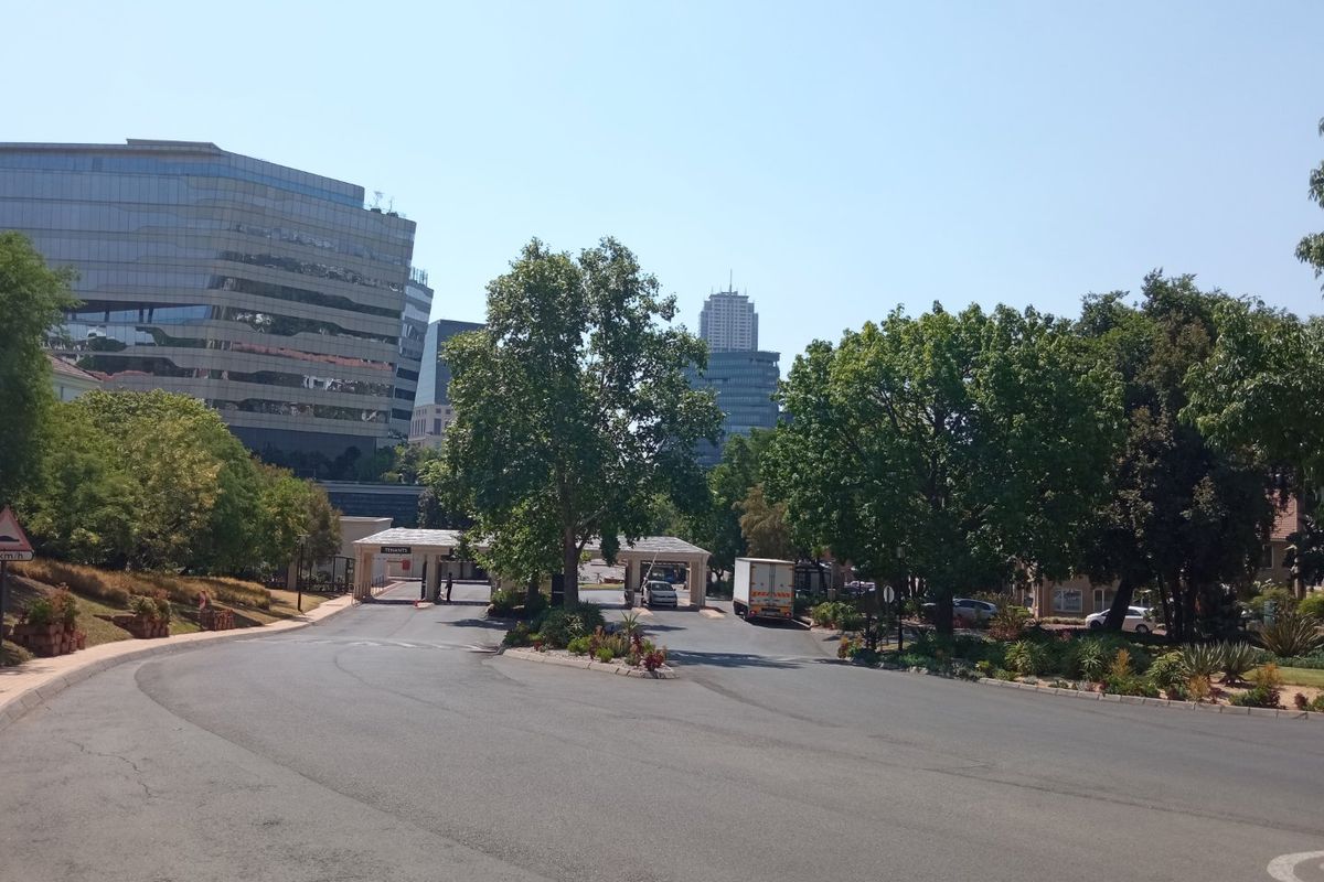 View of the office park entrance featuring a security gatehouse, paved access roads, and established landscaping within a professional business district.