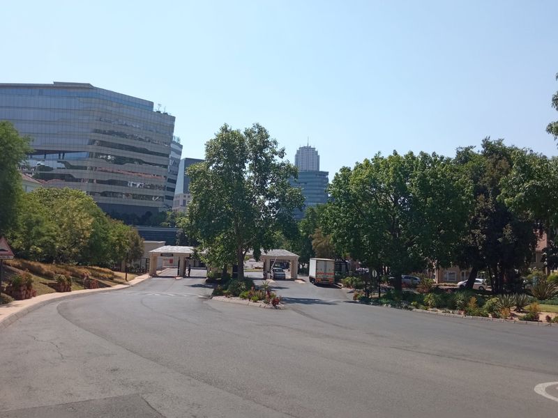 View of the office park entrance featuring a security gatehouse, paved access roads, and established landscaping within a professional business district.
