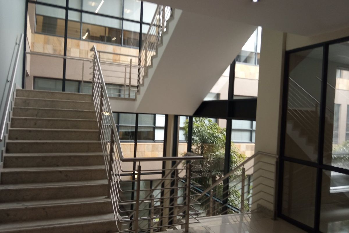 Modern office building atrium featuring a stone staircase with stainless steel balustrades and expansive glass curtain walls providing natural light.