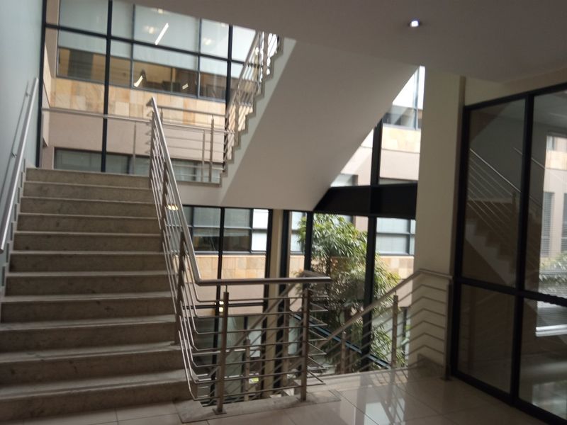 Modern office building atrium featuring a stone staircase with stainless steel balustrades and expansive glass curtain walls providing natural light.