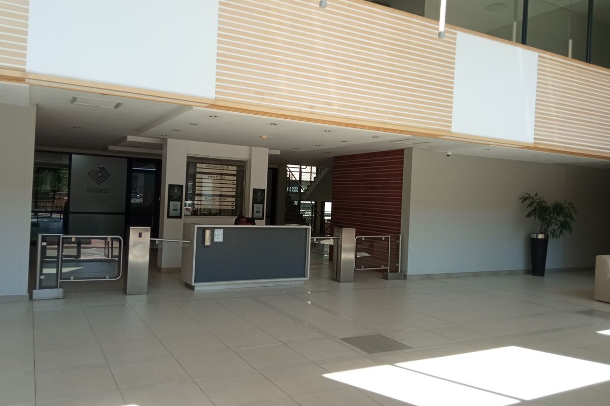 Modern office building entrance lobby featuring a reception desk, security turnstiles, directory signage, and high-quality tiled flooring with timber wall accents.