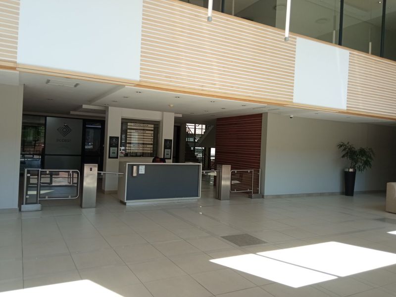 Modern office building entrance lobby featuring a reception desk, security turnstiles, directory signage, and high-quality tiled flooring with timber wall accents.