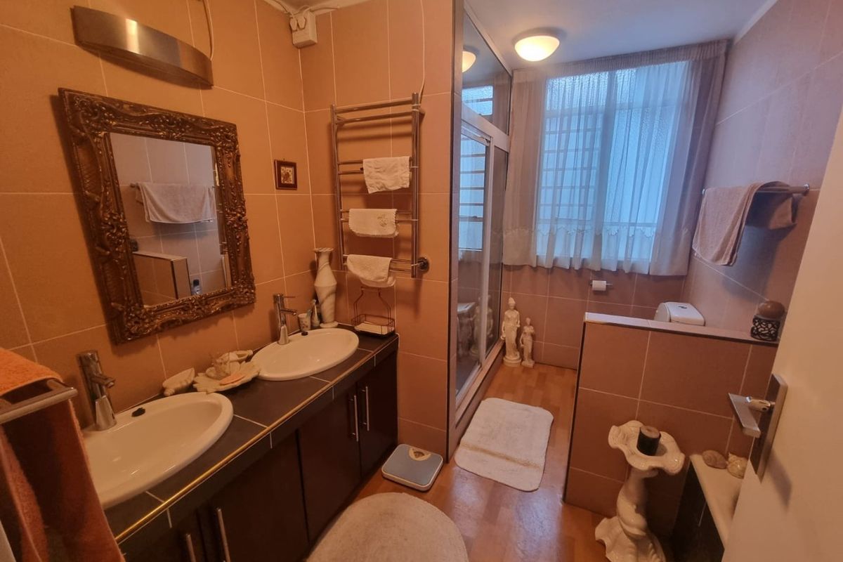 A functional bathroom featuring a double vanity with integrated sinks, a glass-enclosed shower, and a wall-mounted heated towel rail.