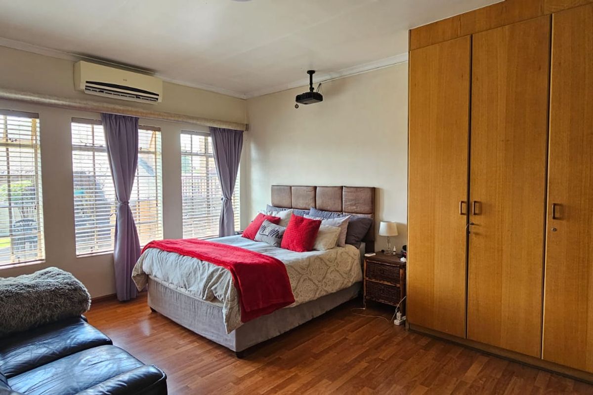 Spacious bedroom featuring built-in wooden wardrobes, laminate flooring, and a wall-mounted air conditioning unit.