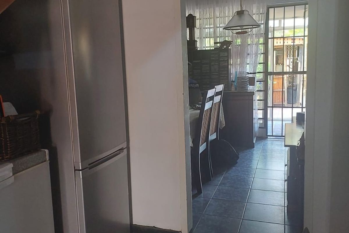 A view from a tiled kitchen area looking through a doorway towards a dining space with a security gate leading to the exterior.