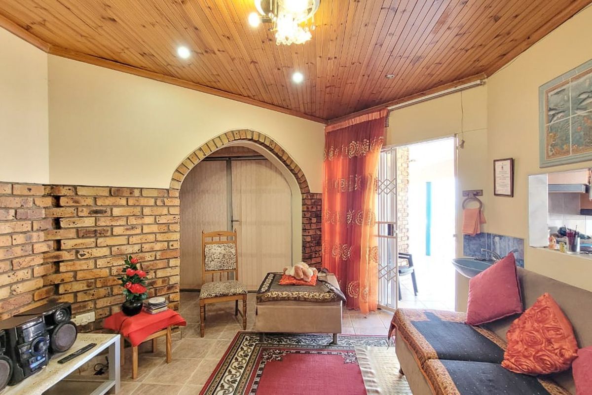 A living room featuring a vaulted timber ceiling, exposed brick feature wall, and an arched doorway leading to an outdoor patio area.