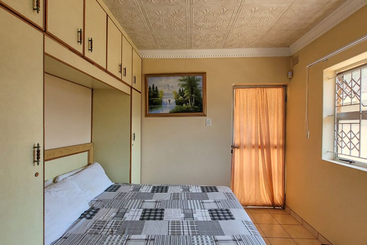 A bedroom featuring built-in cabinetry, tiled flooring, and a window with security bars, offering functional storage and natural light.
