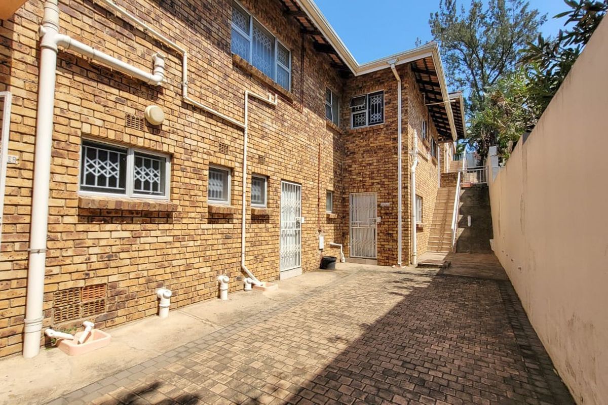 A view of the rear exterior of the property featuring face-brick walls, paved courtyard area, security gates, and an external staircase leading to the upper level.