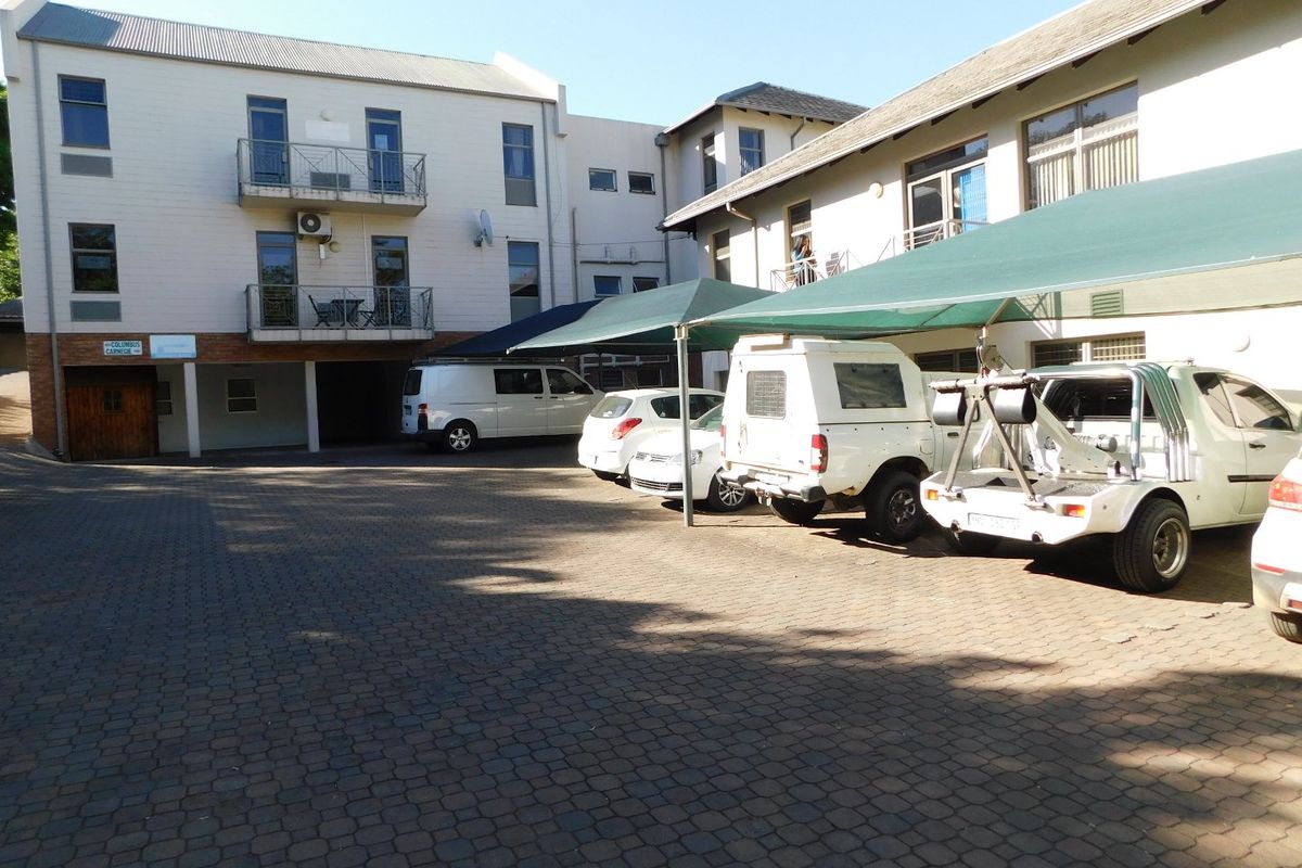 Exterior view of the office building featuring a paved parking area with shade cloth carports and multi-level office units with balconies.