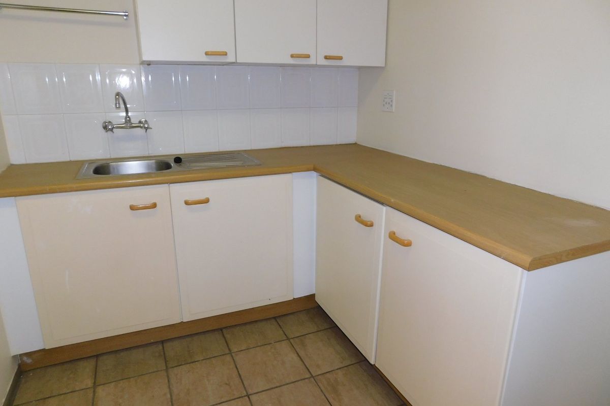 A functional kitchenette area featuring white cabinetry, a stainless steel sink, tiled backsplash, and durable floor tiling.