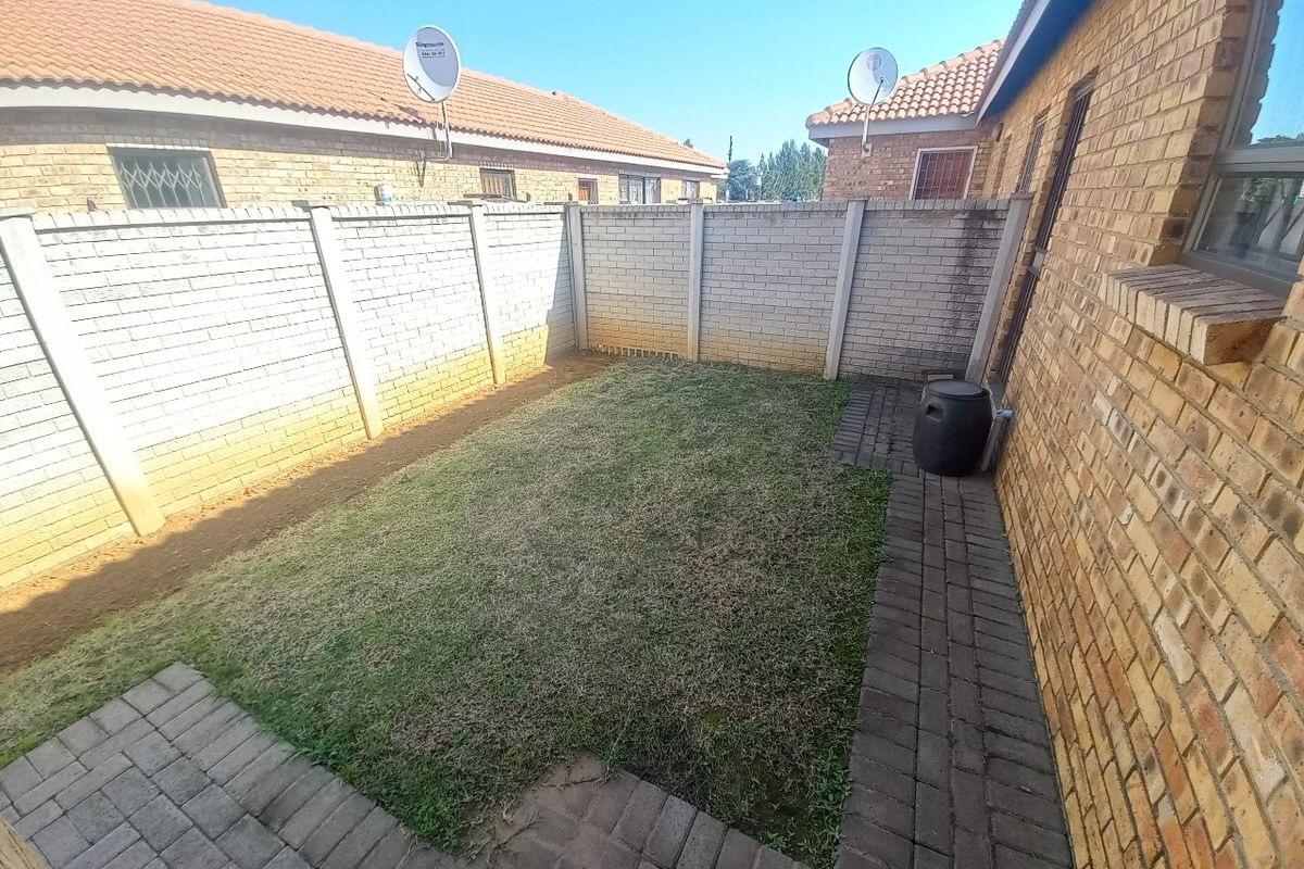 A private rear courtyard featuring a small lawn area, paved walkway, and high brick boundary walls for added privacy.