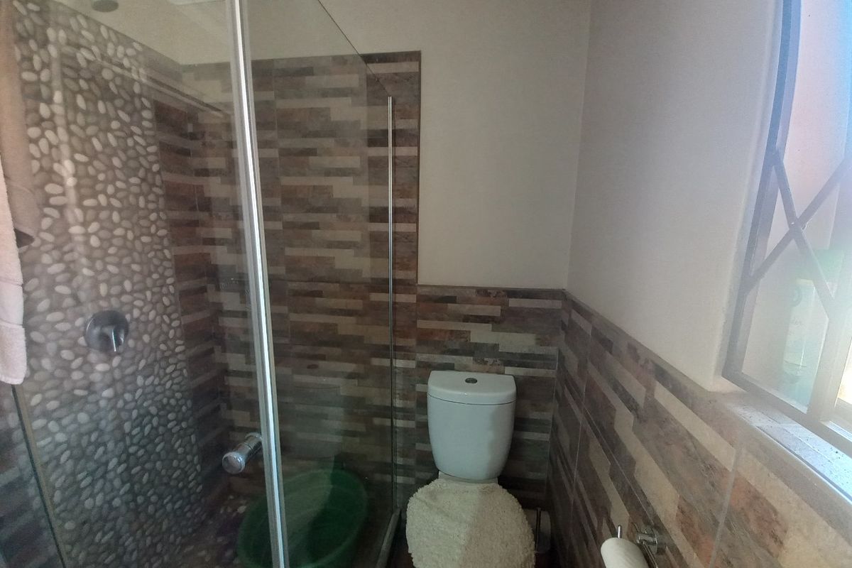 A functional bathroom featuring a glass-enclosed shower with decorative pebble-style tiling and a standard toilet.