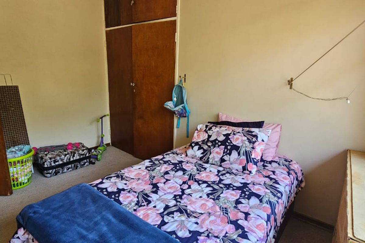 A bedroom featuring built-in wooden cupboards, carpeted flooring, and a window with security bars.
